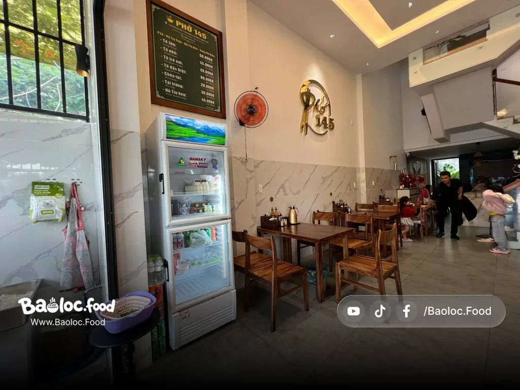 Không gian trong nhà sạch sẽ tại Phở 145 Bảo Lộc với bàn ghế gỗ và khu vực ngồi gọn gàng
